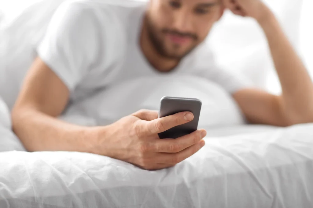 Primer plano de un hombre usando el celular desde la cama