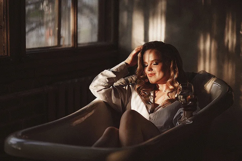 Mujer posando en una bañera con luz cálida, fotografía con estética cinematográfica y tono sensual elegante estilo OnlyFans.